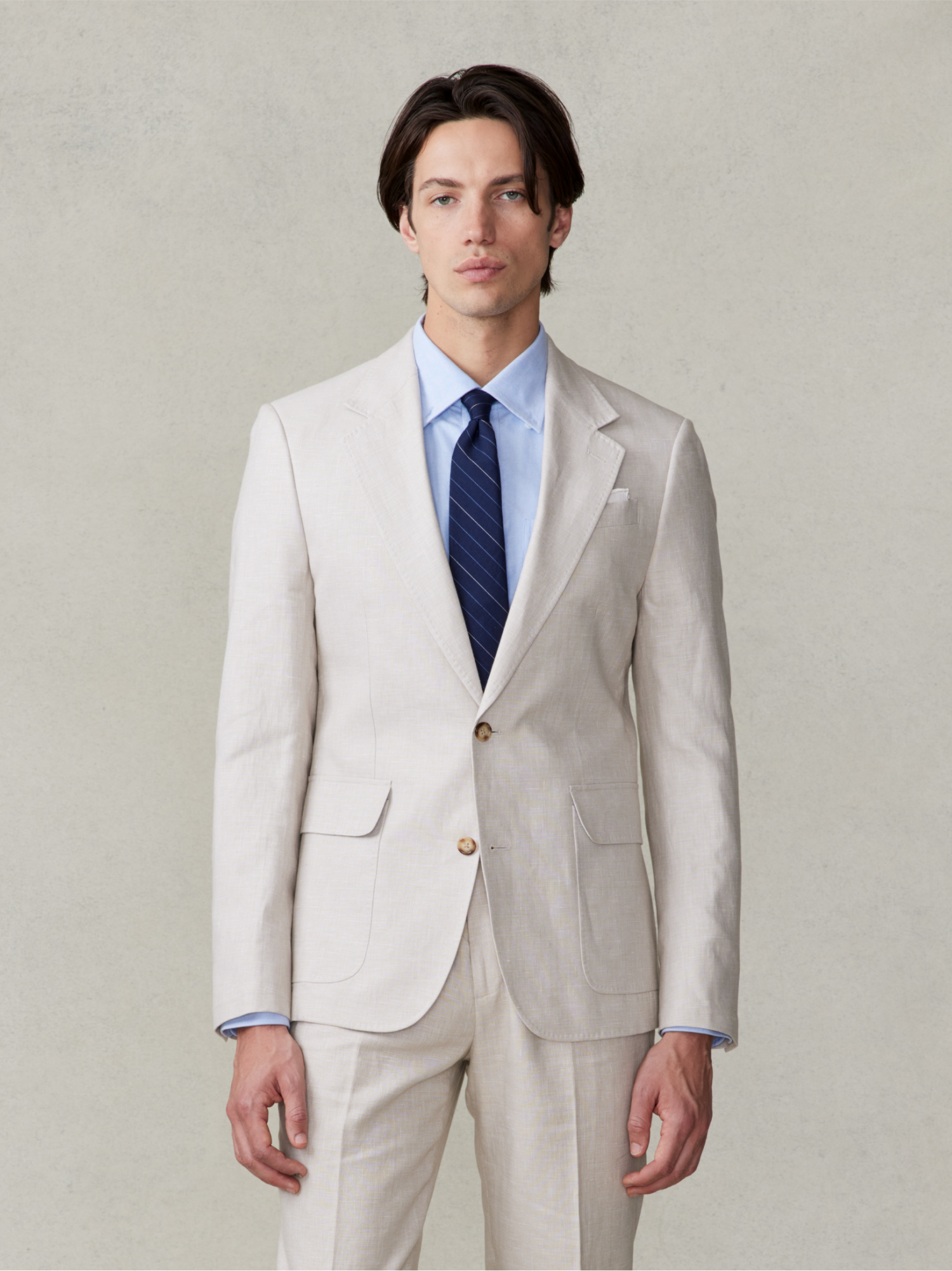 Man in a light beige suit with a blue shirt and dark tie.