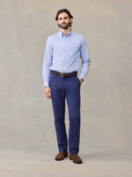 Man in navy chino pants and light blue striped shirt, hand in pocket, full length