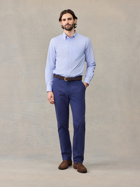 Man in navy chino pants and light blue striped shirt, hand in pocket, full length