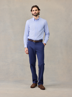Man in navy chino pants and light blue striped shirt, hand in pocket, full length