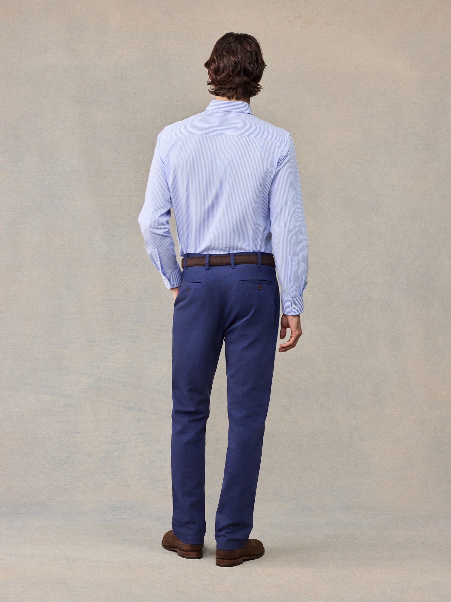 Back view of man in navy chino pants and light blue striped shirt, full length