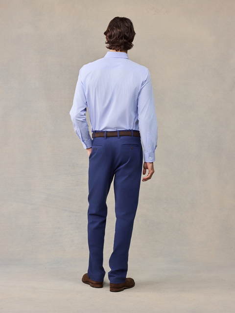 Back view of man in navy chino pants and light blue striped shirt, full length
