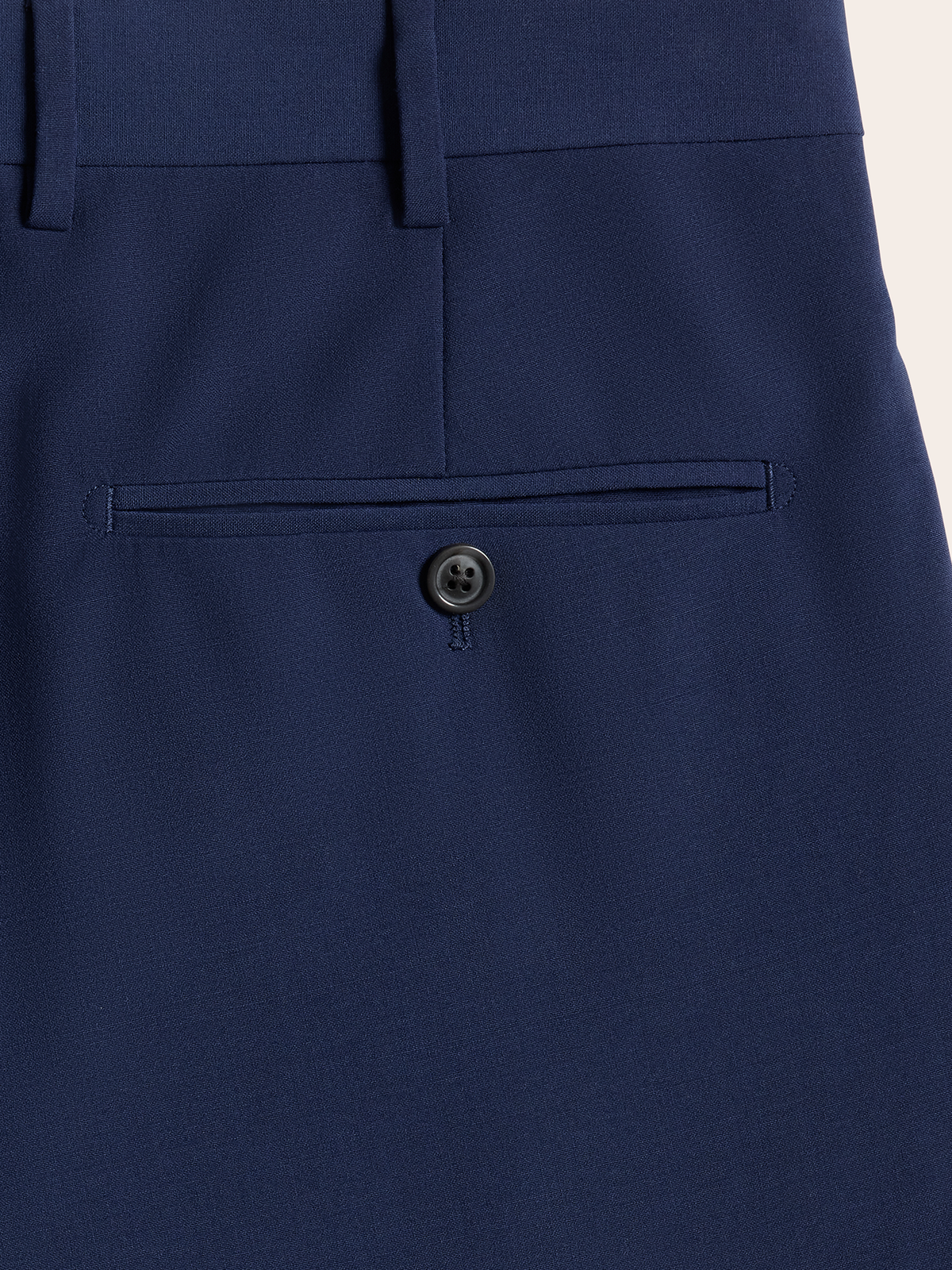Close-up of a cove blue suit pants back welt pocket with button.