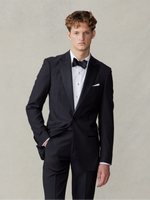 Man wearing a black tuxedo with a bow tie and white shirt, standing against a neutral background.