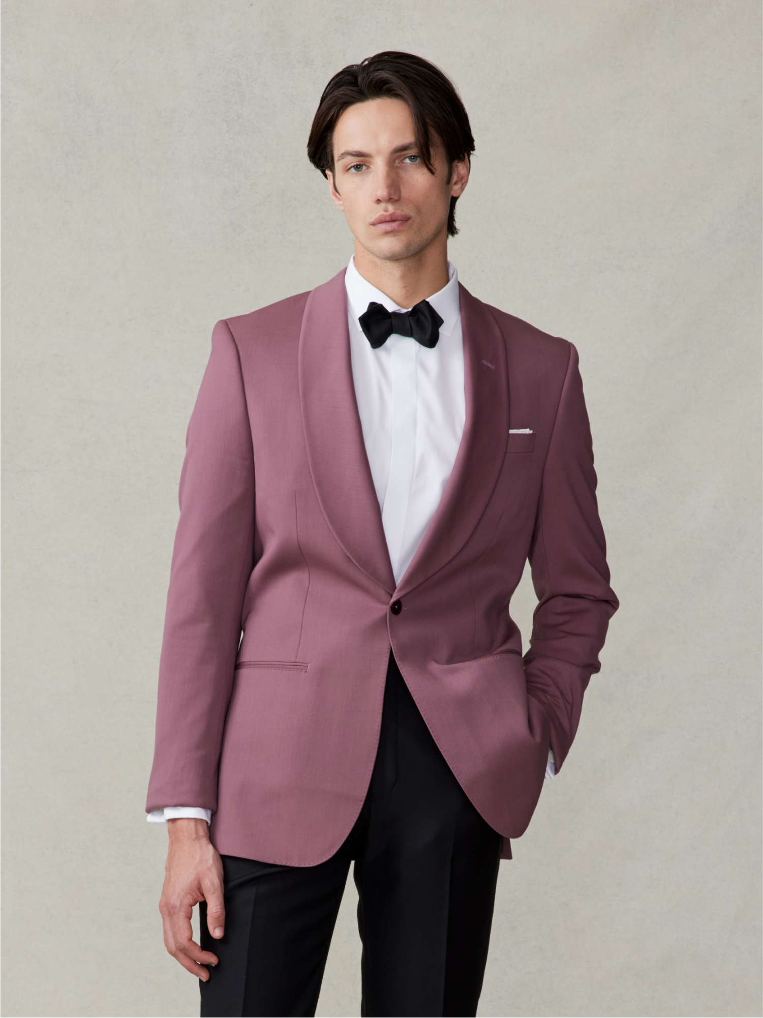 Man wearing a pink tuxedo jacket with a black bow tie and black pants.