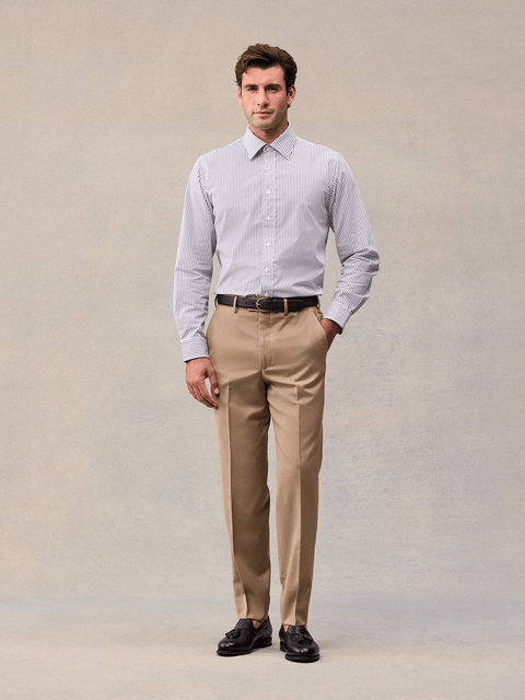 Model in camel flat-front suit trousers with a black belt and striped dress shirt, front view.