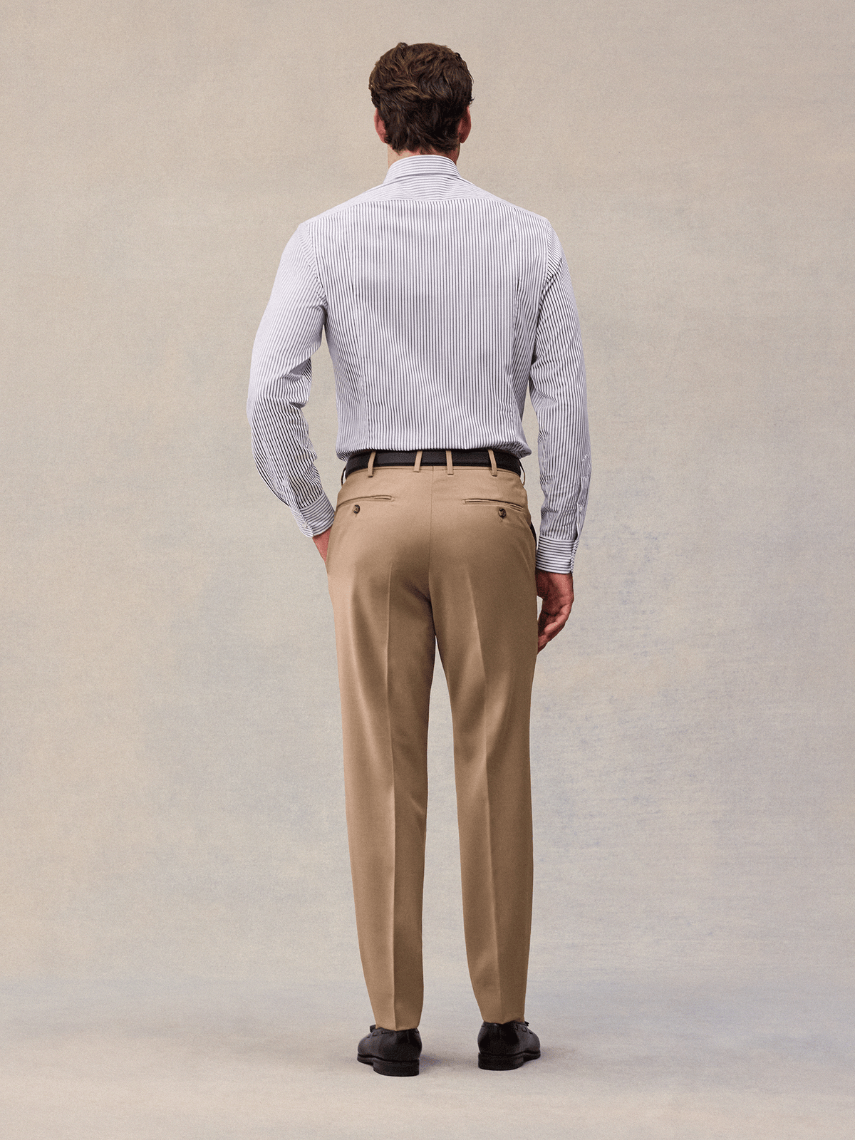 Back view of camel suit trousers with back welt pockets, worn with a black belt.