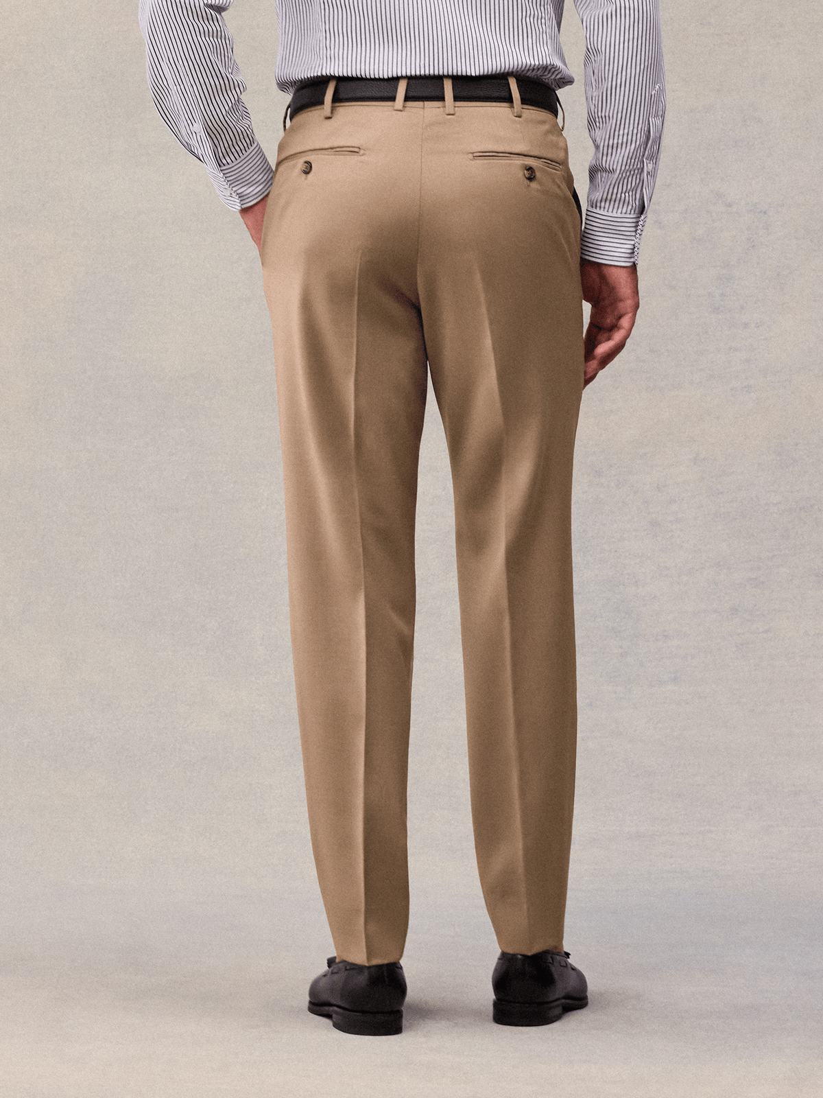 Close-up of camel suit trousers from the back, showing buttoned welt pockets.