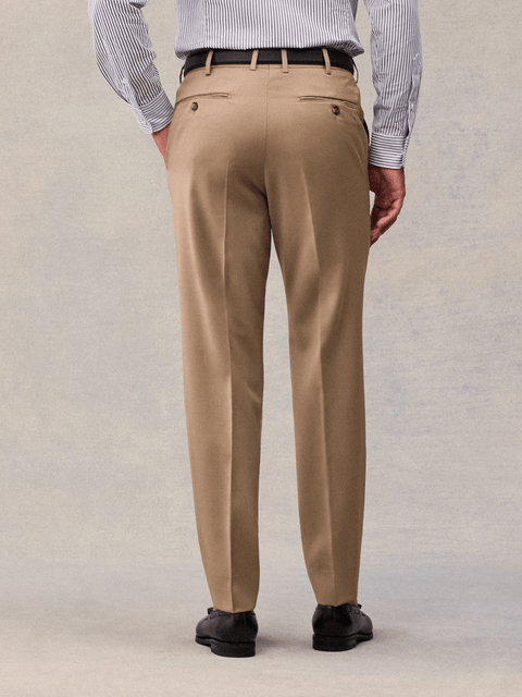 Close-up of camel suit trousers from the back, showing buttoned welt pockets.
