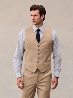Model in a camel suit vest with button front and four welt pockets over a striped shirt.