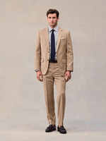 Model facing forward in a camel two-button suit with navy tie and white pocket square.