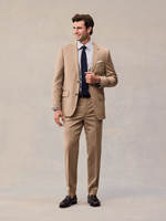 Full-length view of a model in a camel two-button suit with navy tie and black tassel loafers.