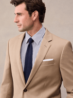 Close-up of a camel suit jacket's notch lapel with white pocket square and navy knit tie.