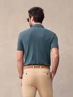 Back view of man in dusk blue pique polo and khaki chinos against beige backdrop