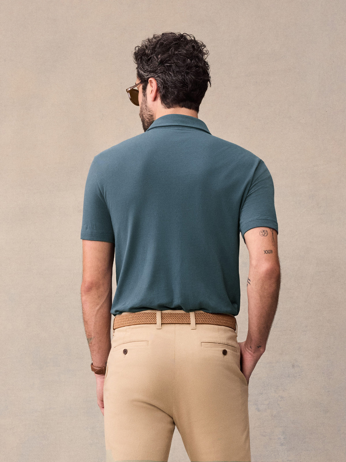 Back view of man in dusk blue pique polo and khaki chinos against beige backdrop