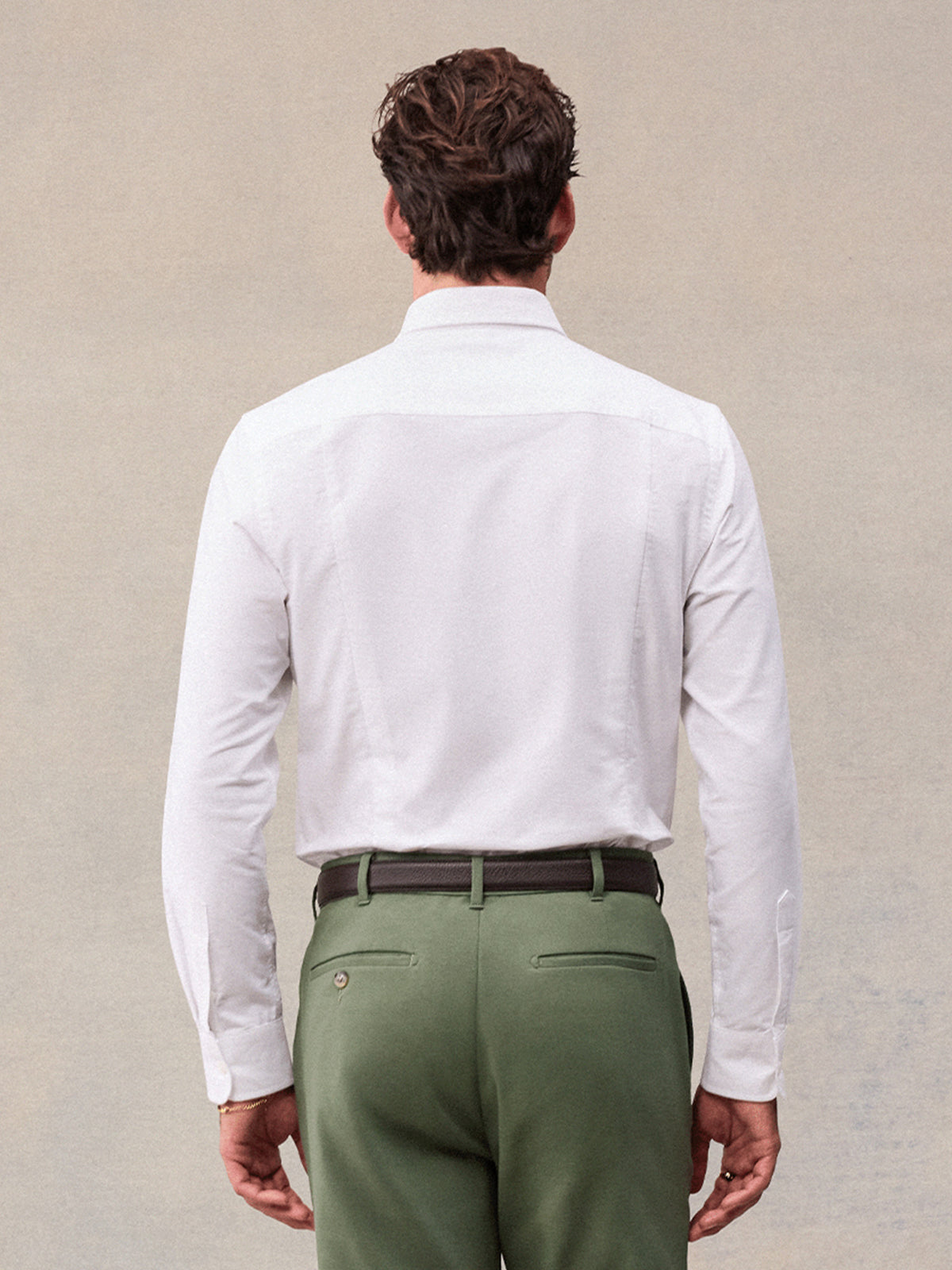 Back view of man in white oxford shirt and olive green trousers, waist-up