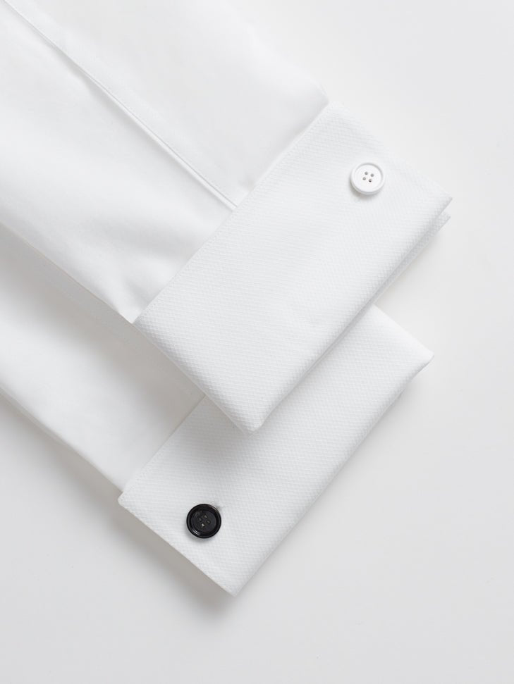 Two white shirt cuffs with buttons, one white and one black.