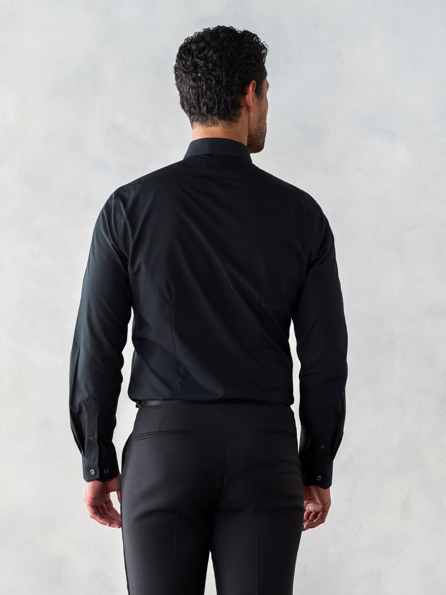 Man wearing a black dress shirt and pants, viewed from the back.
