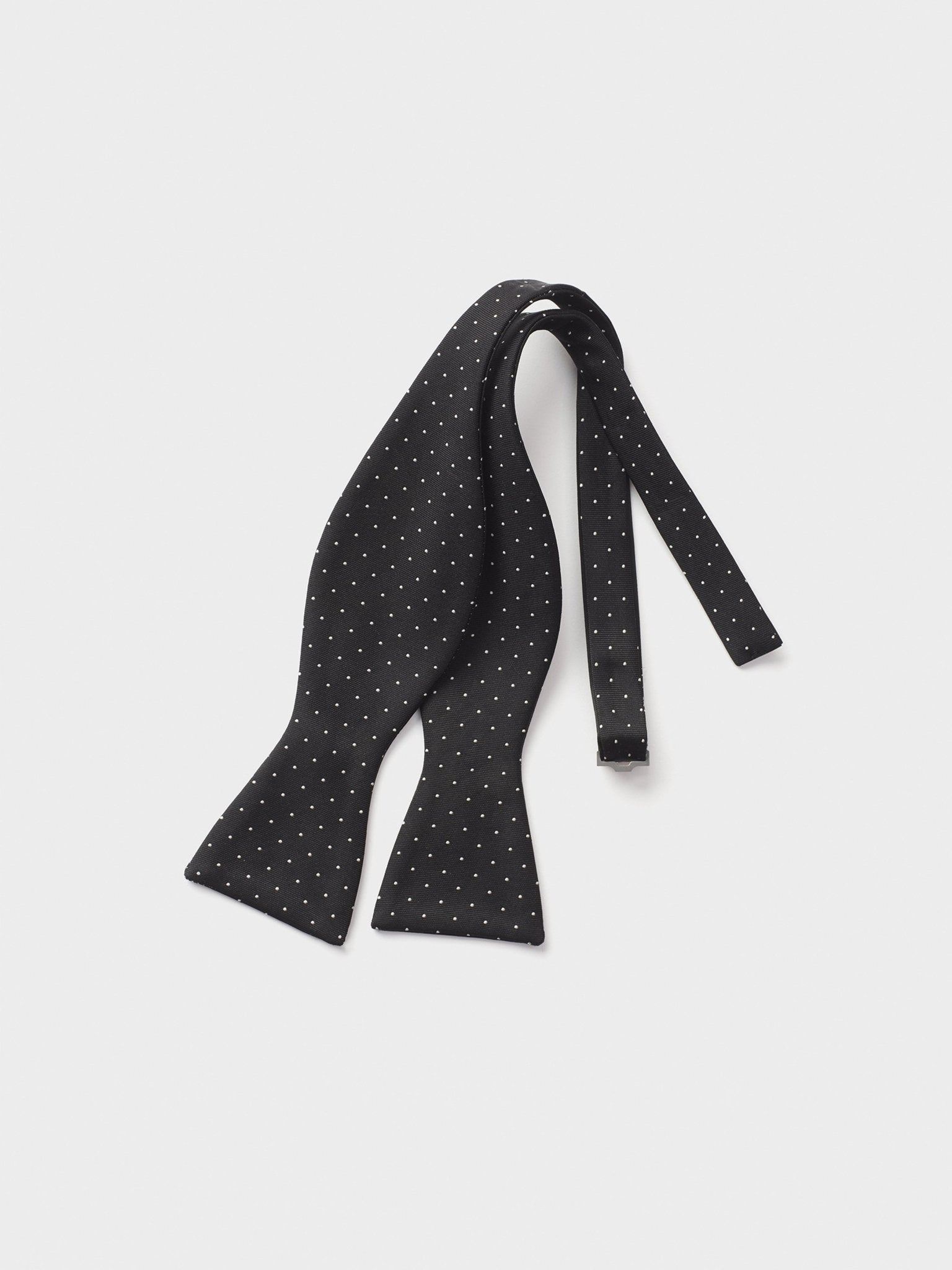 Black bow tie with white polka dots, laid flat on a light background.
