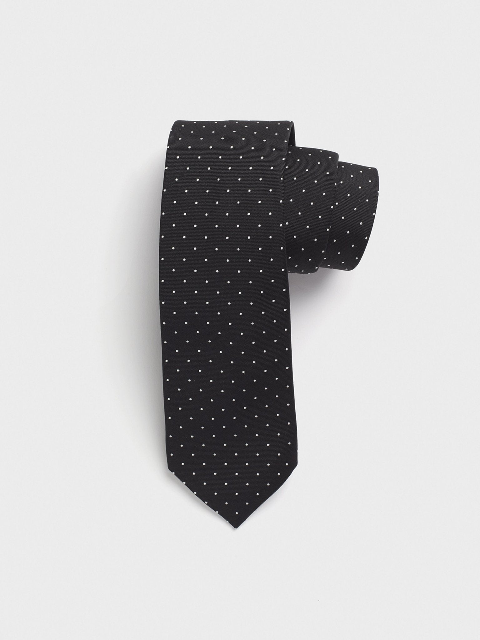 Black tie with white polka dots, rolled up on a white background.