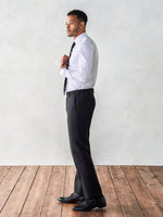 Man in a white shirt and black pants, adjusting his tie, standing on wooden floor.
