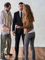 A man in a black suit is being groomed by two stylists.