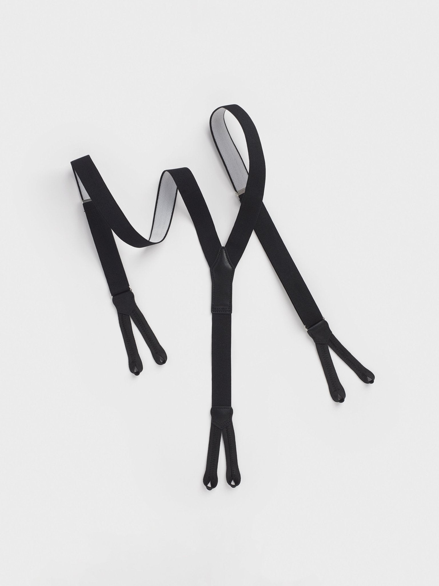Black suspenders with clips on both ends laid flat on a white background.