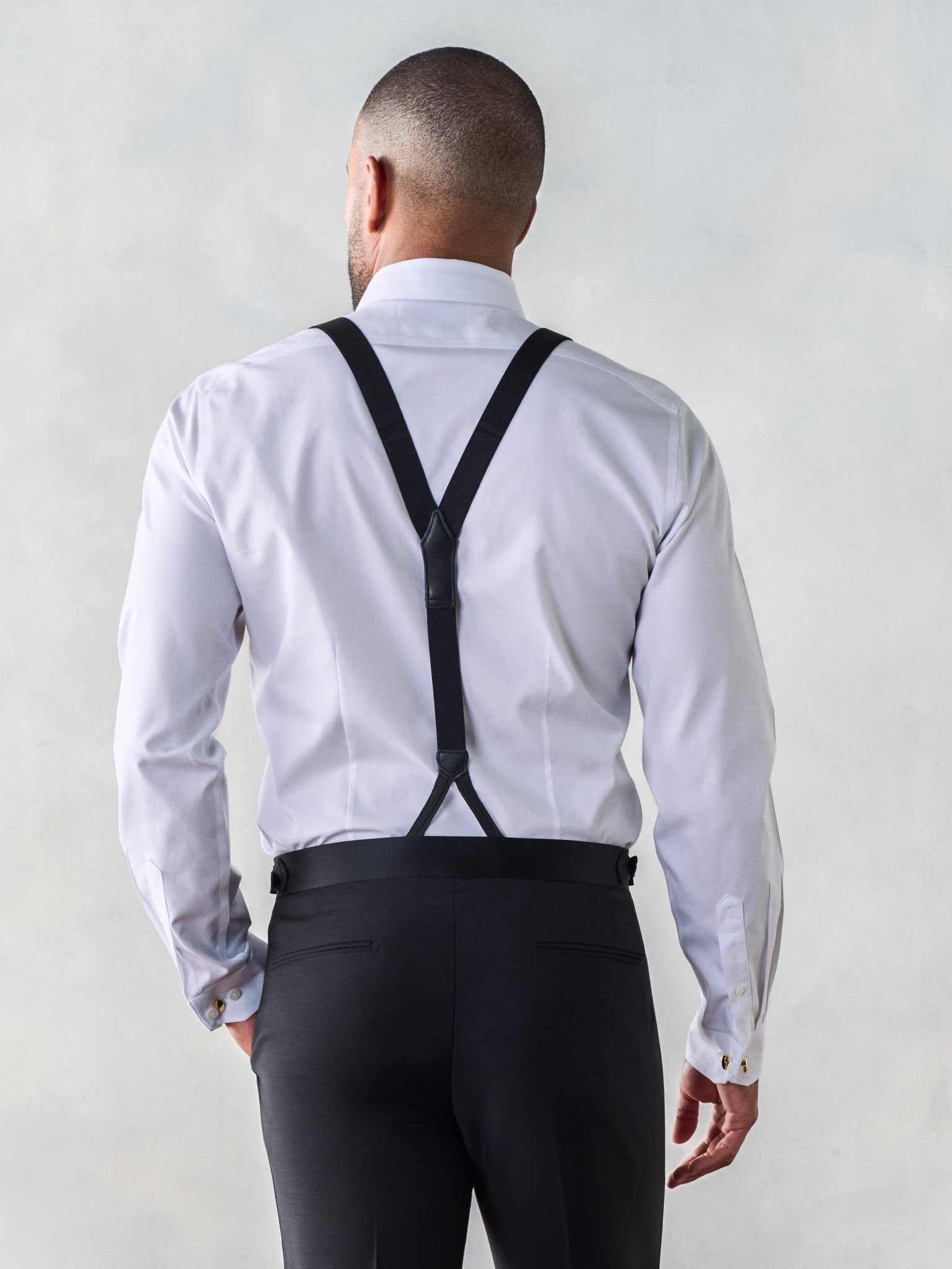 Man wearing a white shirt and black suspenders, viewed from the back.
