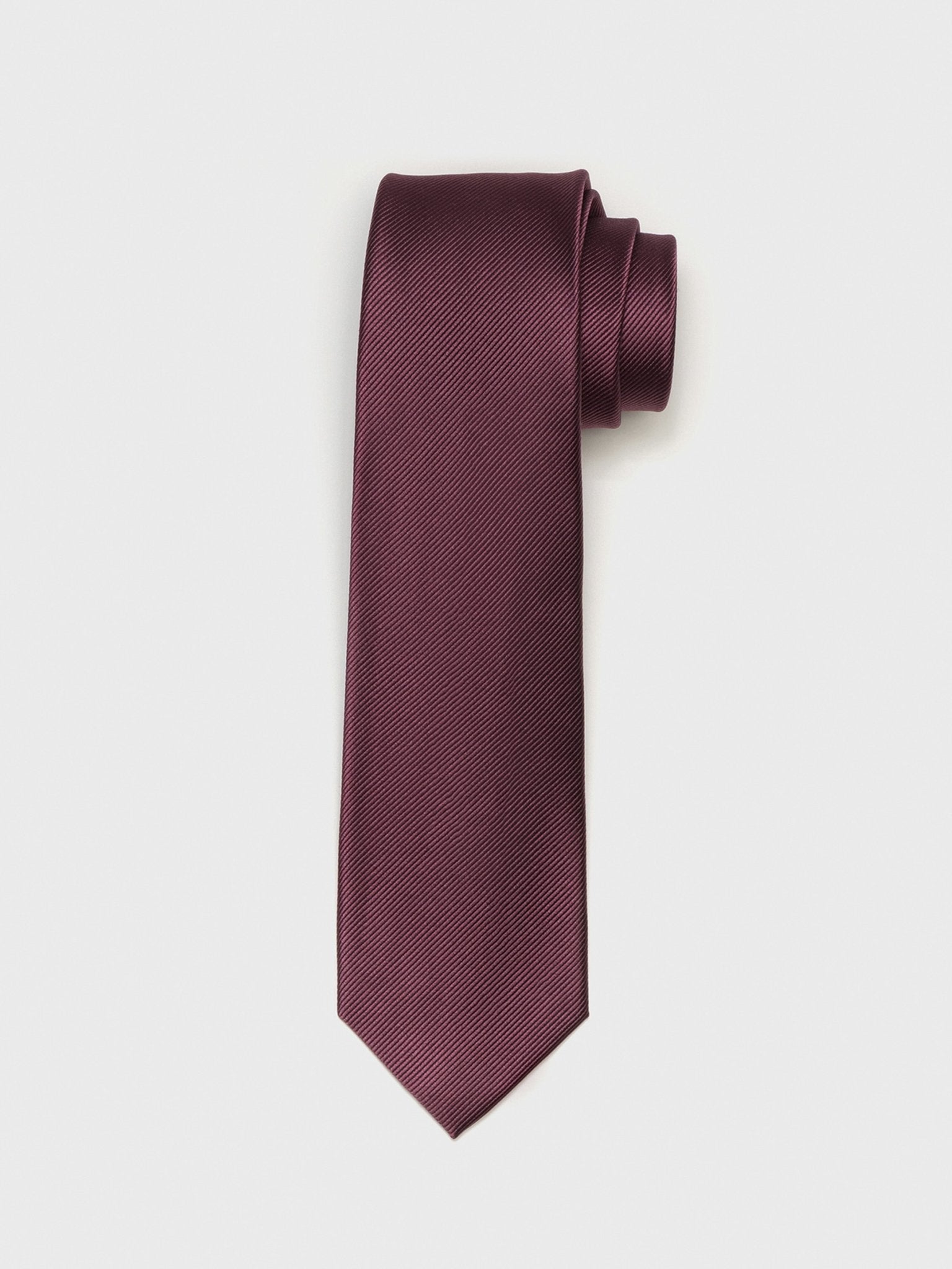 Burgundy tie with a textured pattern, rolled and resting on a white background.