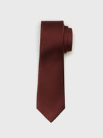 Burgundy tie with a textured pattern, rolled up on a white background.