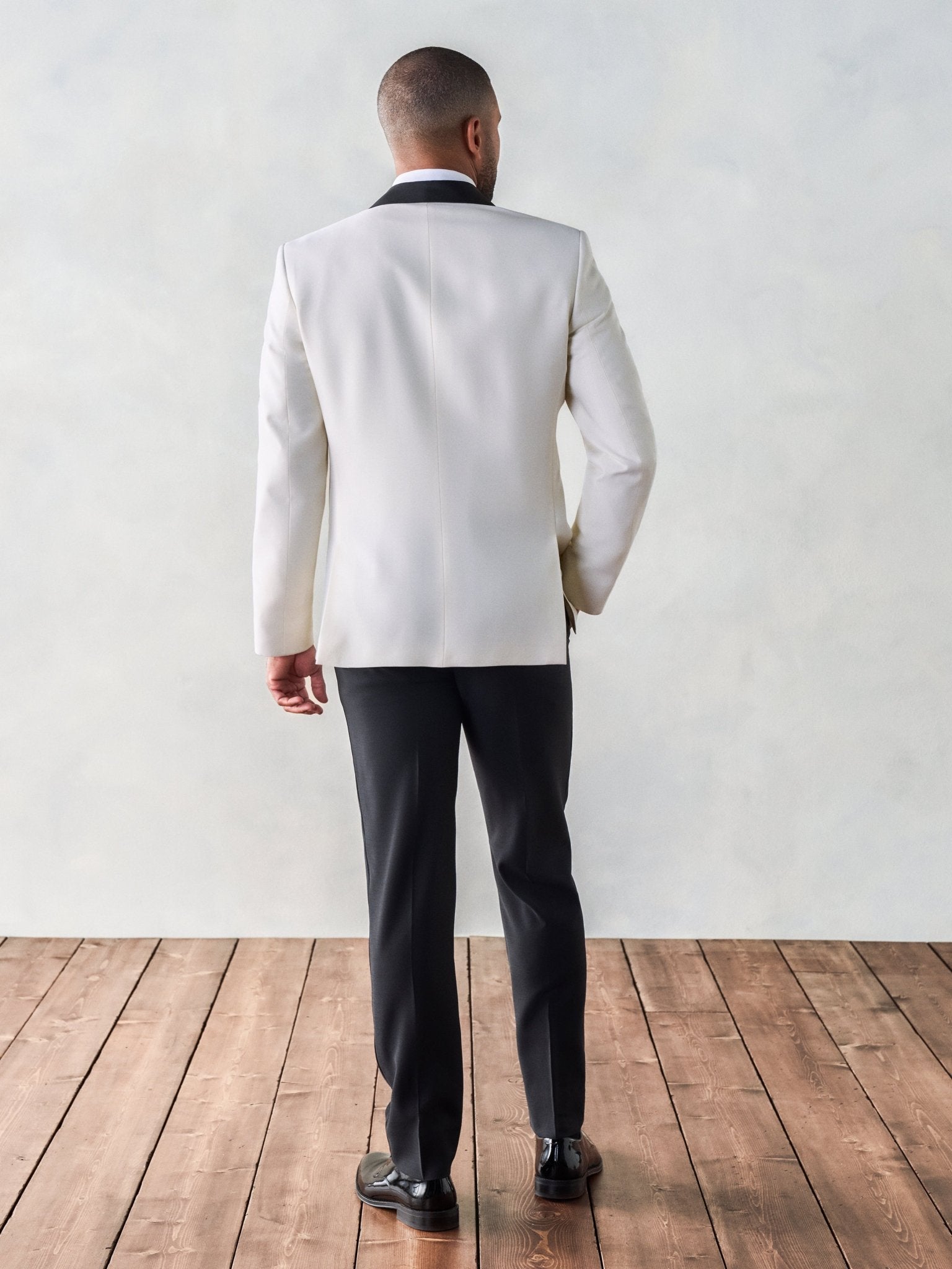 Man in a white tuxedo jacket and black pants, viewed from the back.