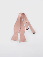 A light pink bow tie with adjustable straps on a white background.