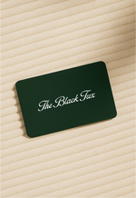 Dark green The Black Tux gift card resting on cream ribbed fabric.