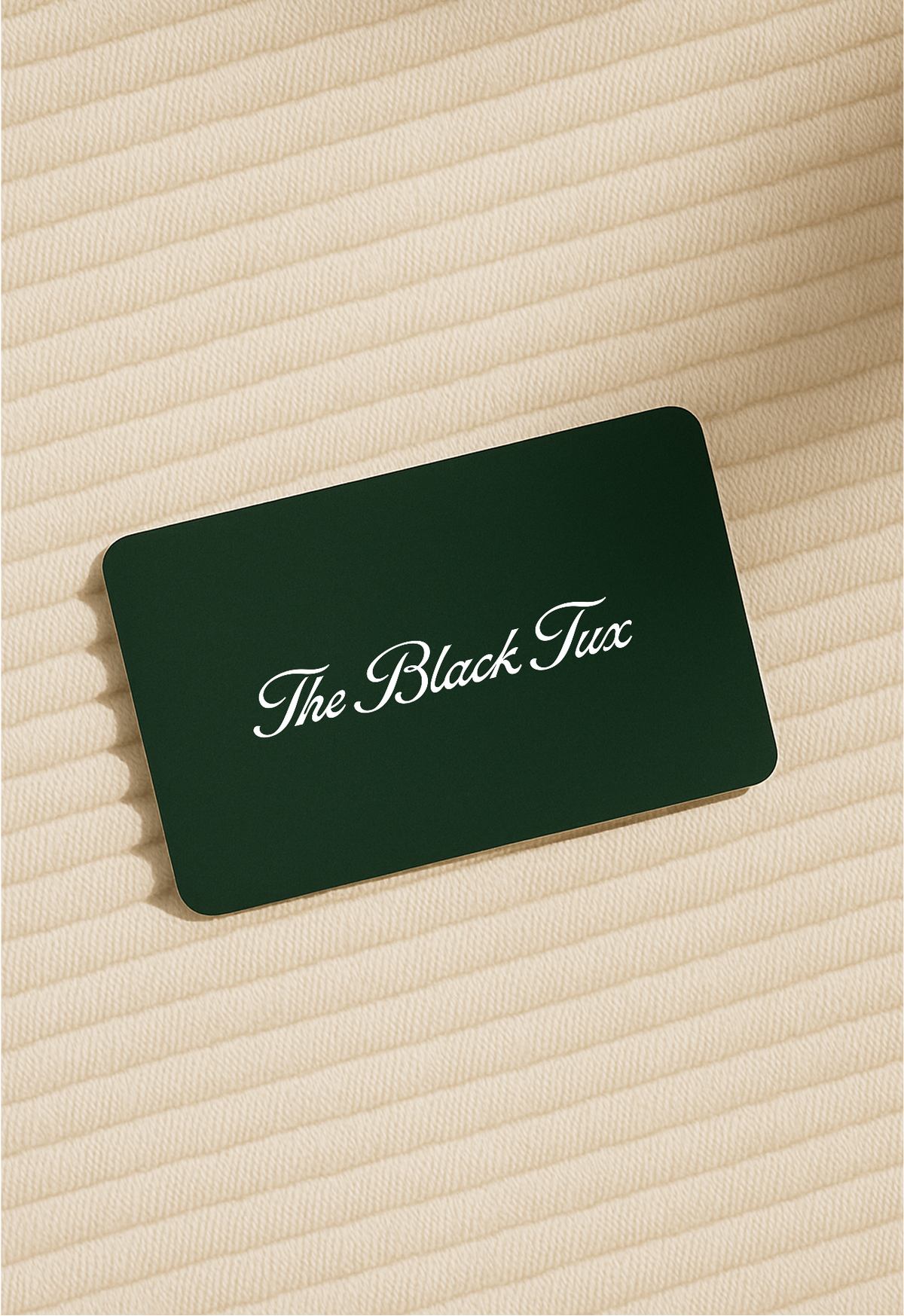 Dark green The Black Tux gift card resting on cream ribbed fabric.