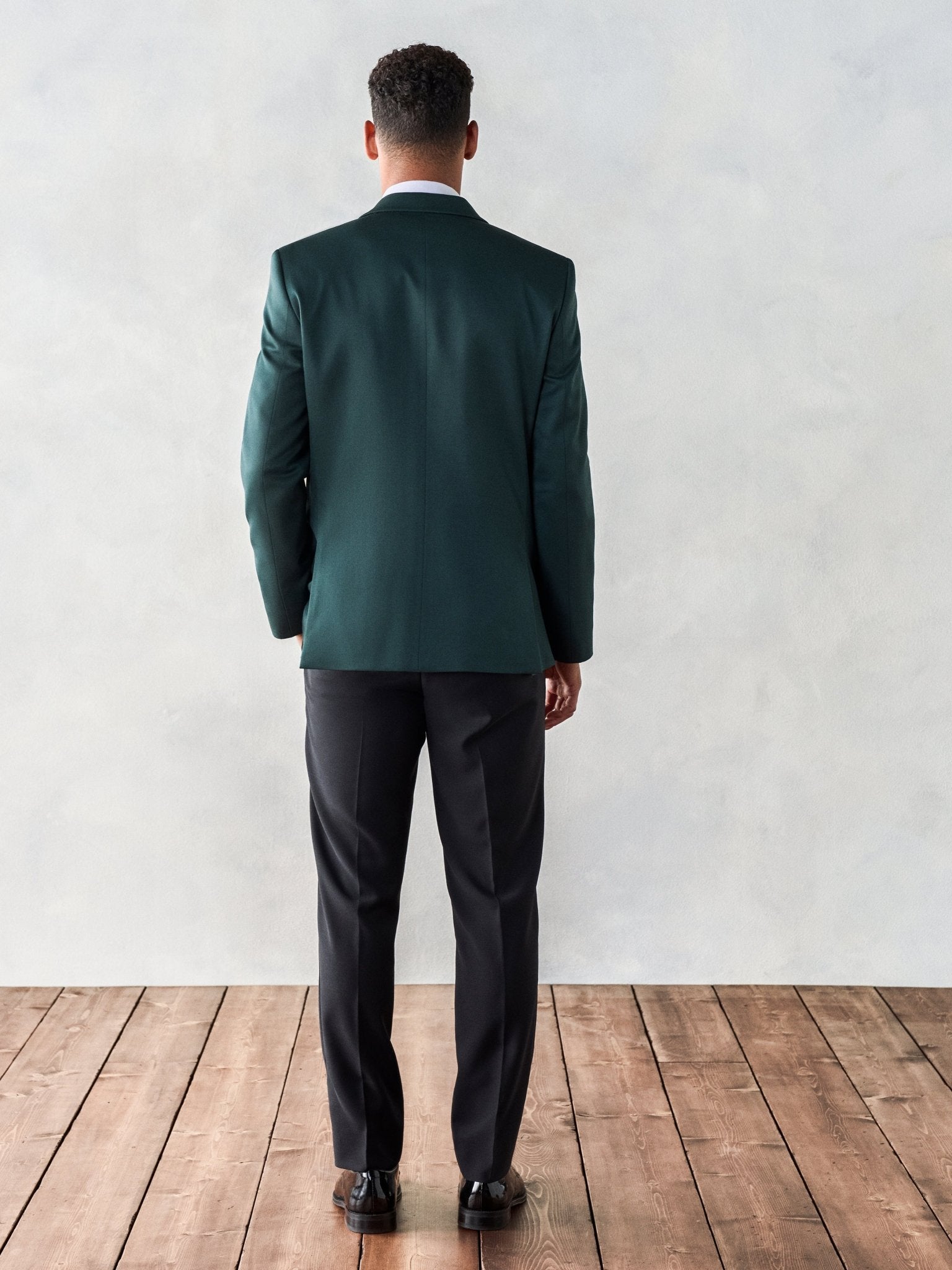 Man wearing a green suit jacket and black pants, viewed from the back.