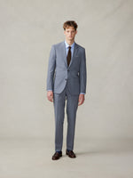 Man wearing a grey suit with a brown tie and brown shoes, standing against a neutral background.