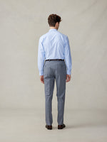 A man in a light blue shirt and grey trousers, viewed from the back.