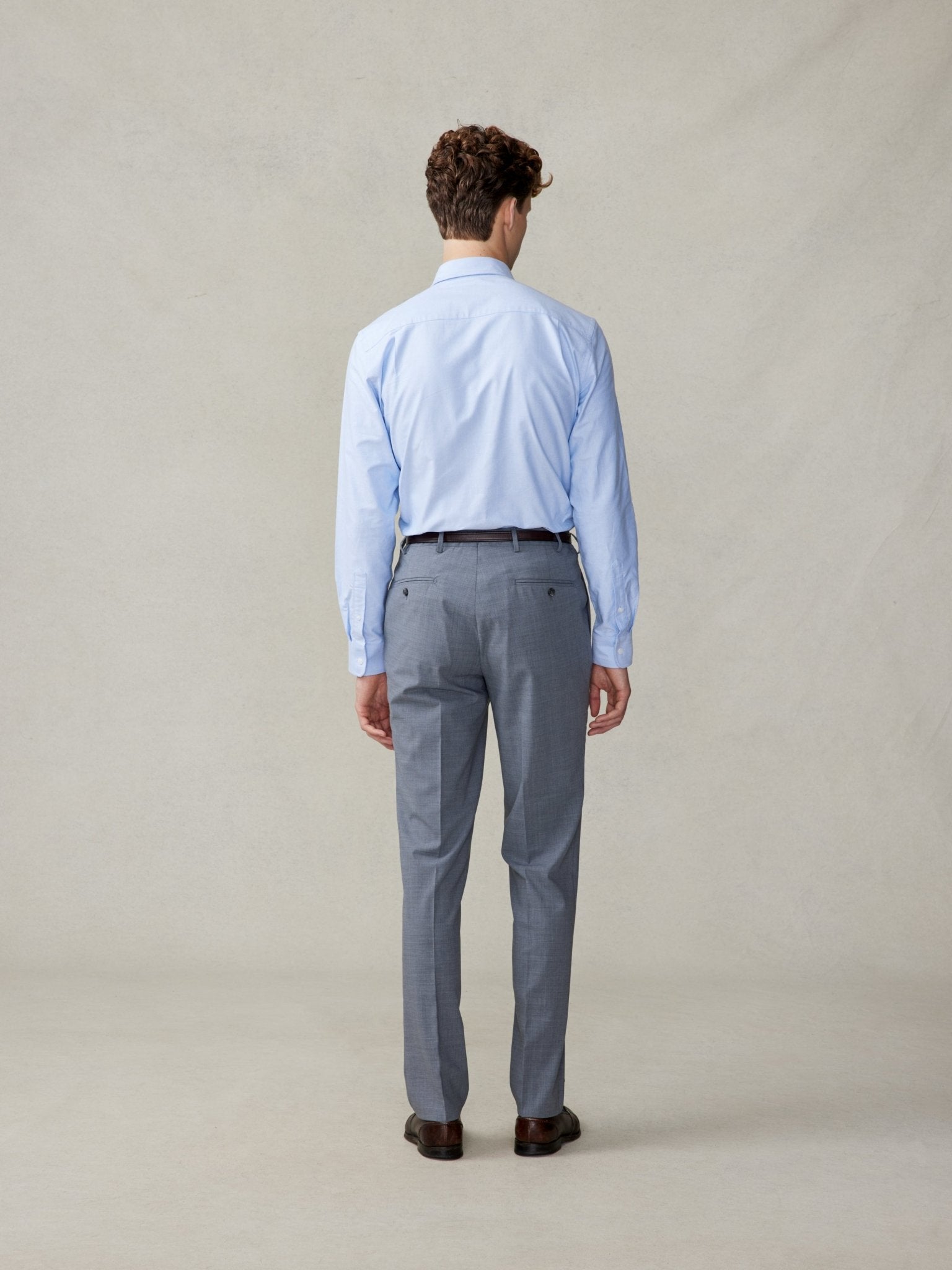 A man in a light blue shirt and grey trousers, viewed from the back.