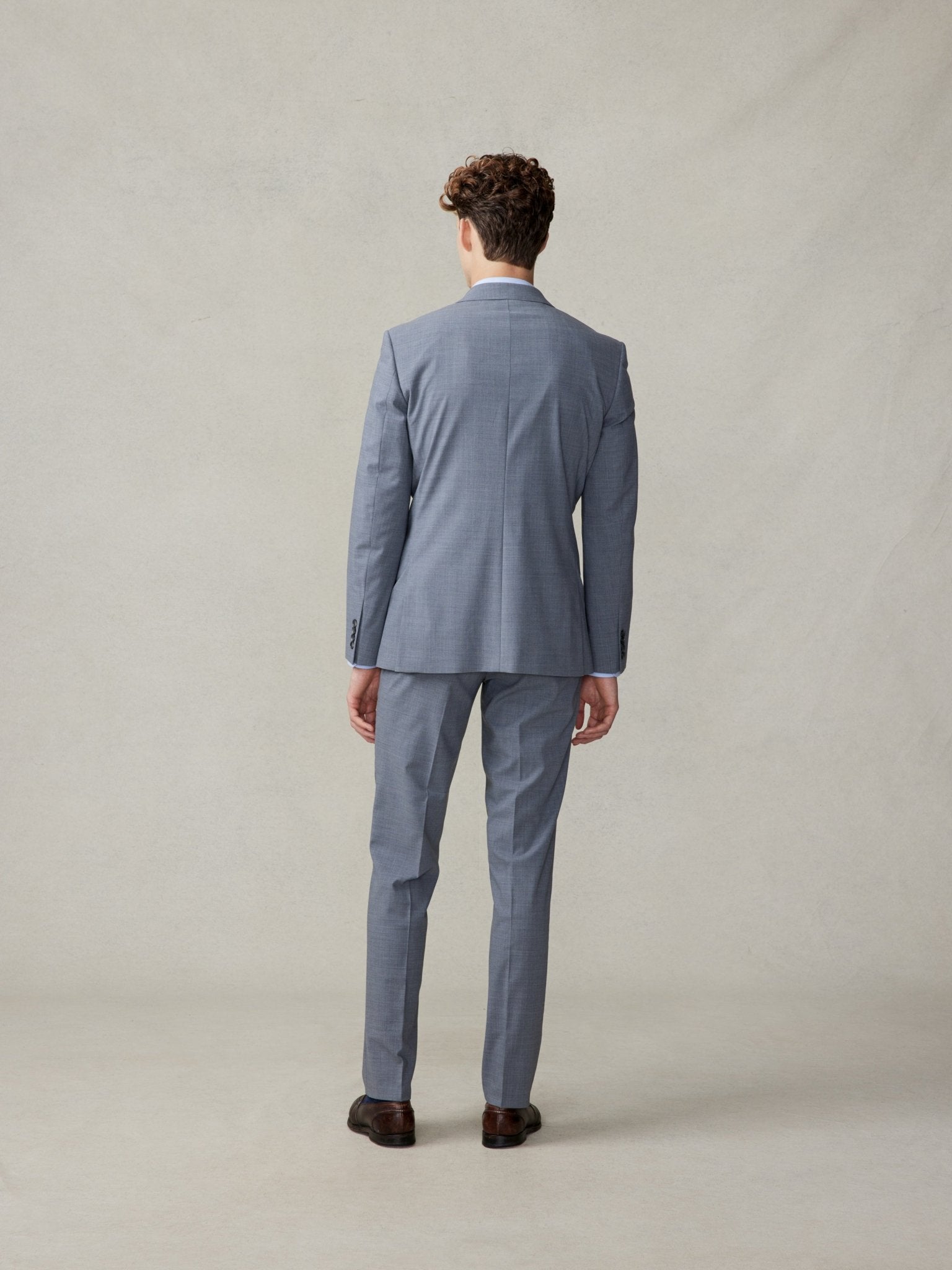 Man in a grey suit viewed from the back, standing on a neutral background.