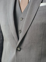 Close-up of a grey suit with a beige tie and buttons visible.