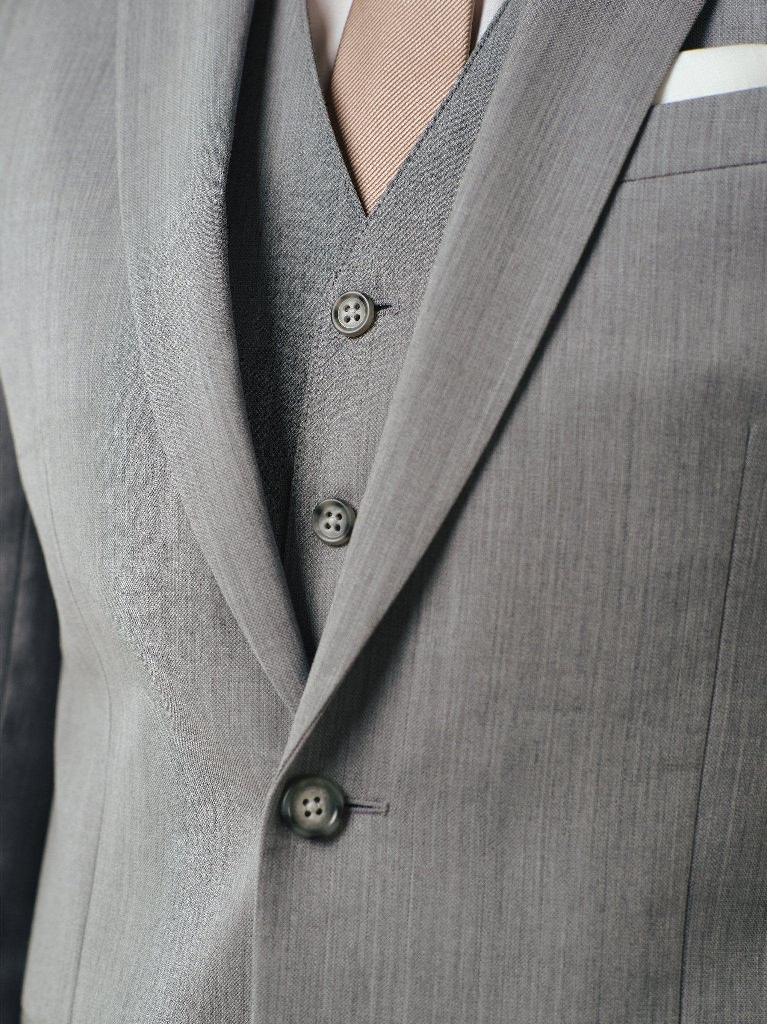 Close-up of a grey suit with a beige tie and buttons visible.