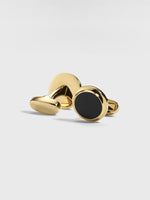 Gold cufflinks with a black circular center on a light background.