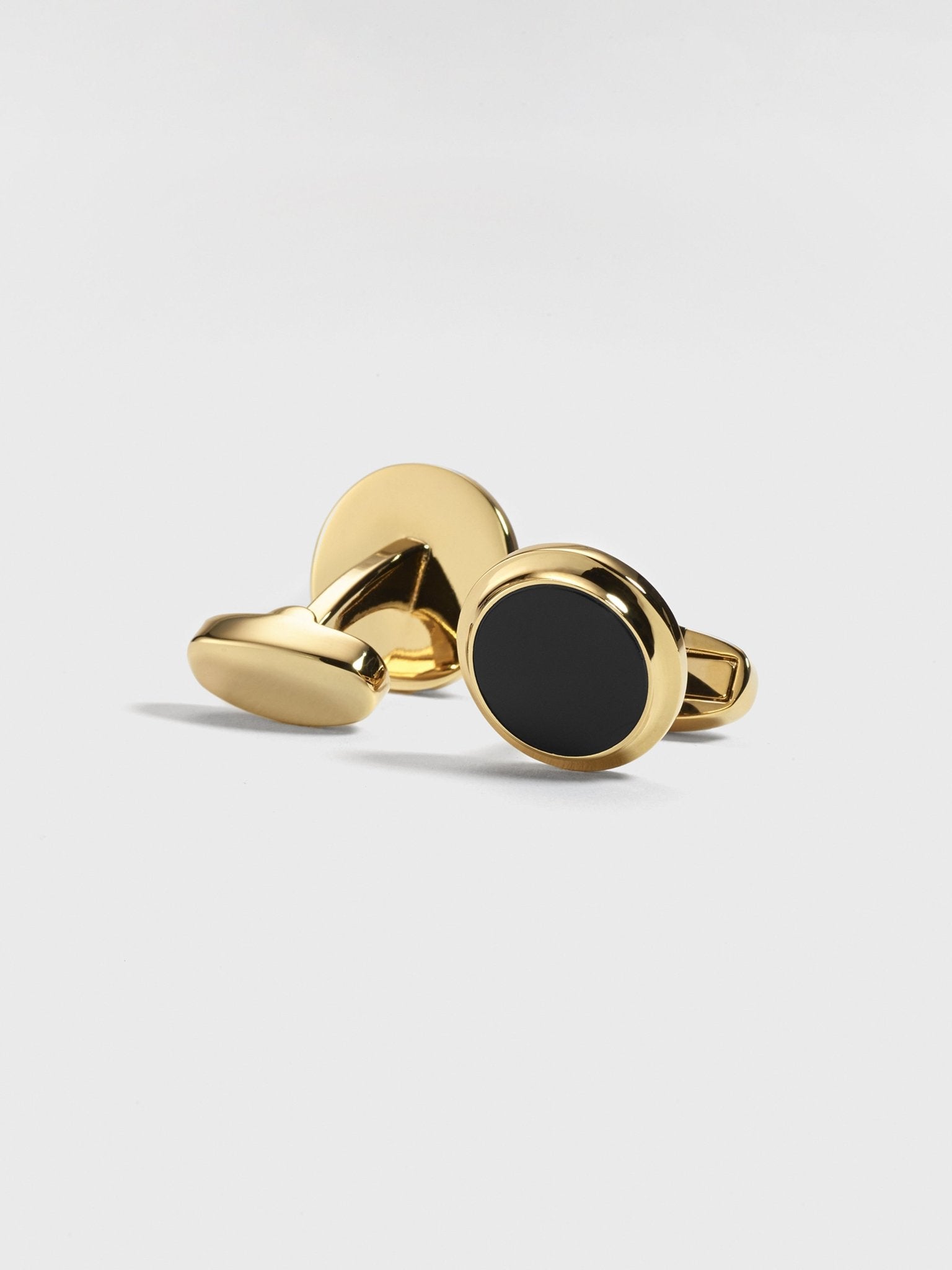 Gold cufflinks with a black circular center on a light background.