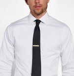 Man wearing a white shirt and a black tie with a gold tie clip.