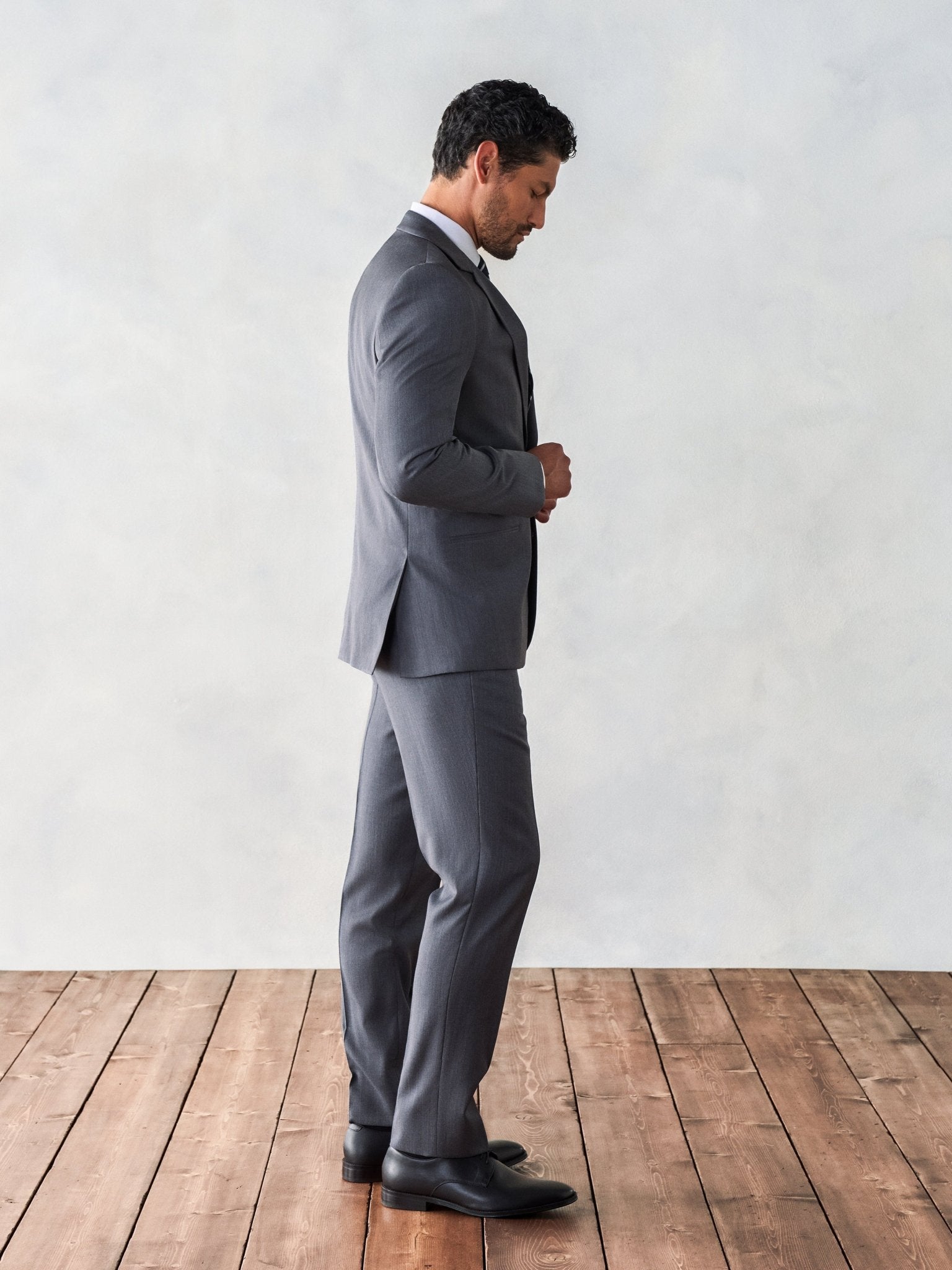Man in a grey suit standing on wooden floor, looking down.