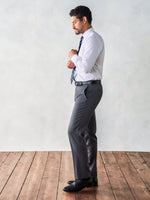 Man adjusting his shirt cuffs while wearing a white shirt and grey trousers.