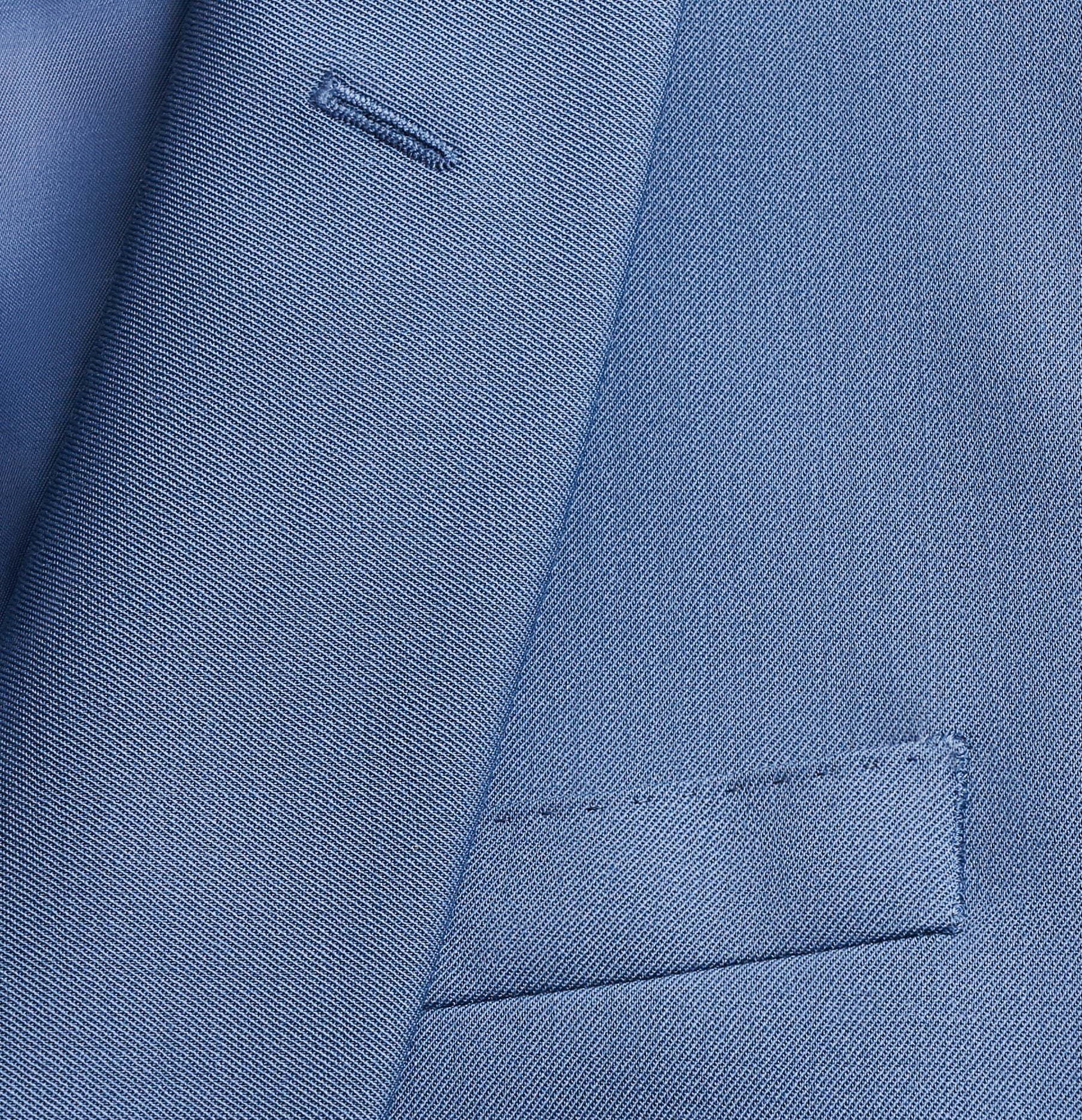 Close-up of a blue suit fabric with a pocket and stitching details.