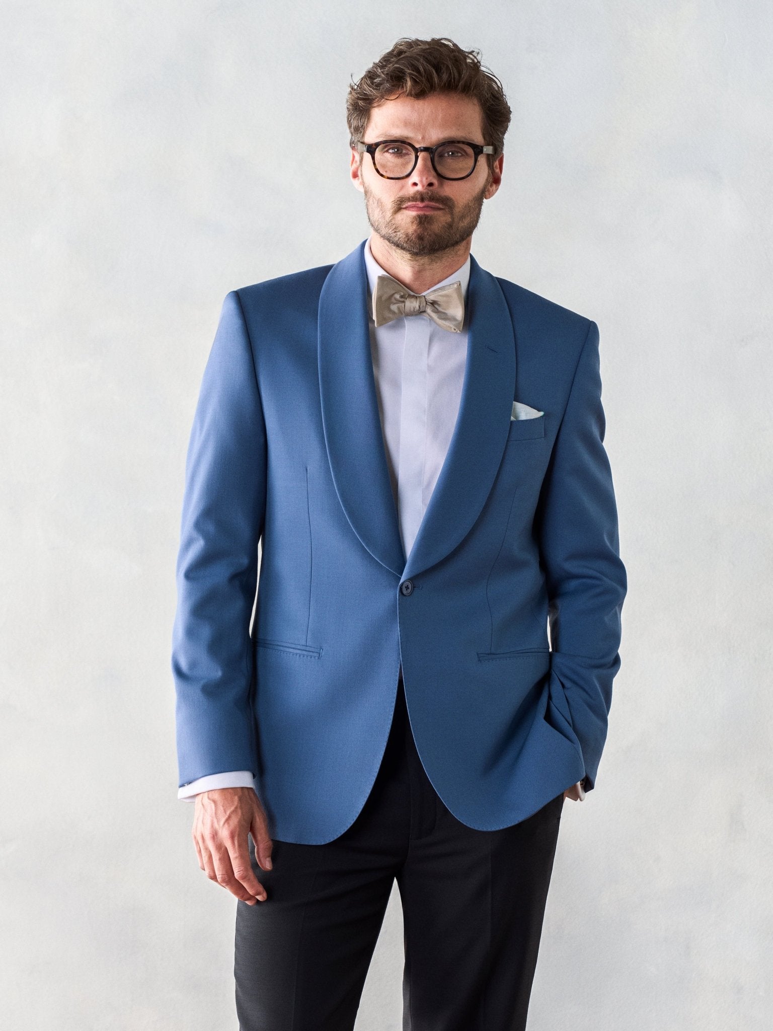 Man wearing a blue tuxedo jacket with a bow tie and glasses.