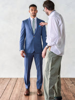 A man in a blue suit is being adjusted by another person.