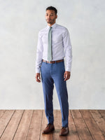 Man in a light shirt and blue pants stands on wooden floor against a light background.